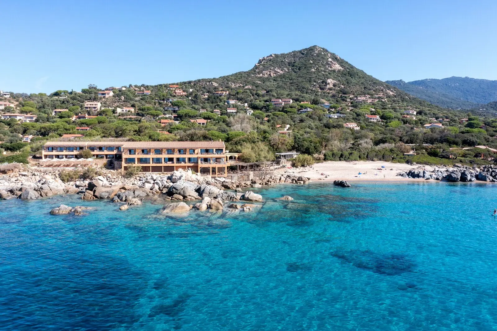 The beachfront hotel seen from the water, between granite rocks and the hillside