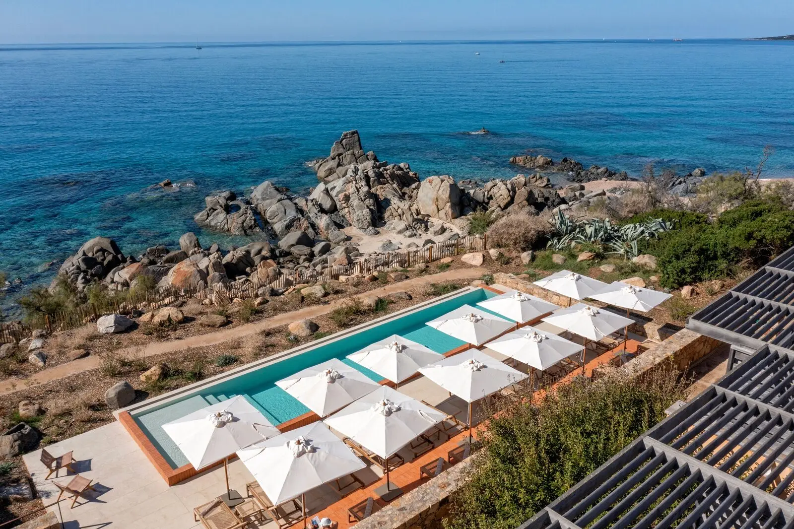 The pool and its white parasols above the rocks and the sea